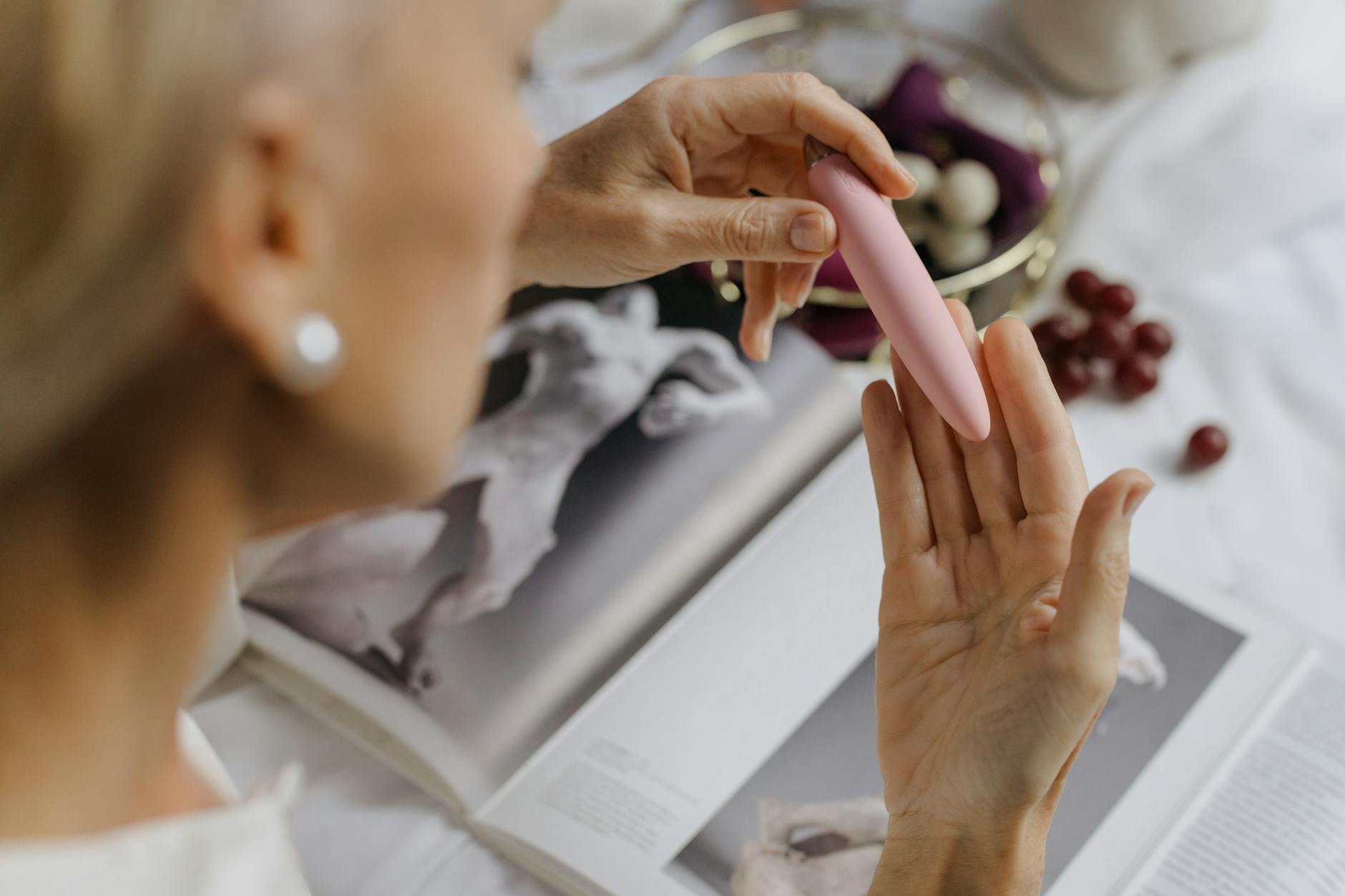 Close-up of a person holding a pink vibrator with art books in the background