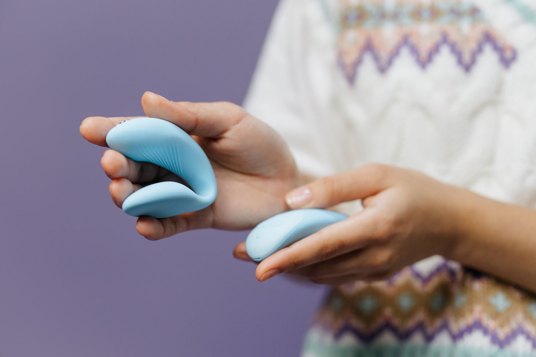 Nahaufnahme: Hände halten einen eleganten blauen klitoralen Vibrator vor violettem Hintergrund