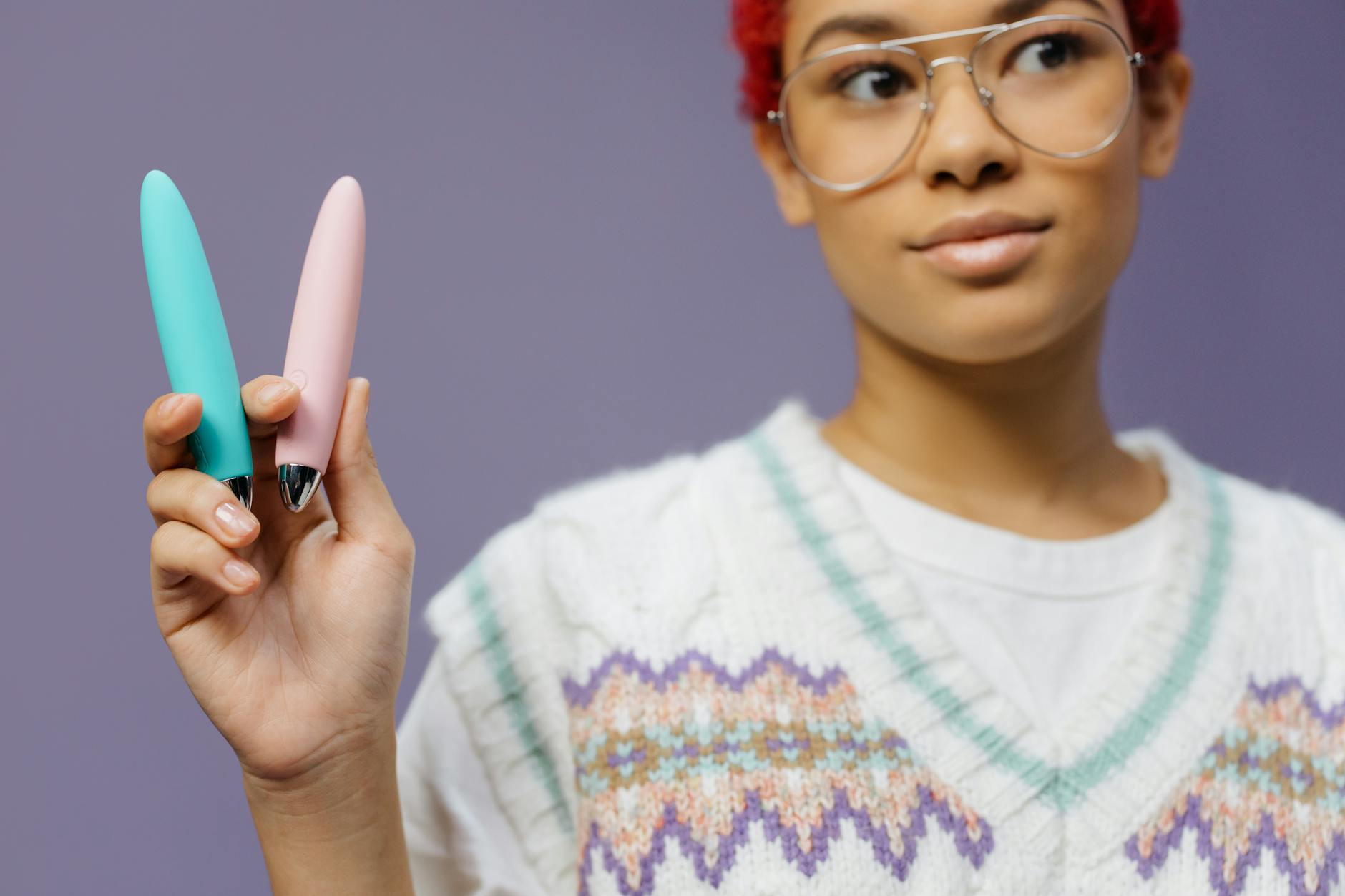 Woman holding two colorful vibrators against a purple background, representing choice and personal agency.