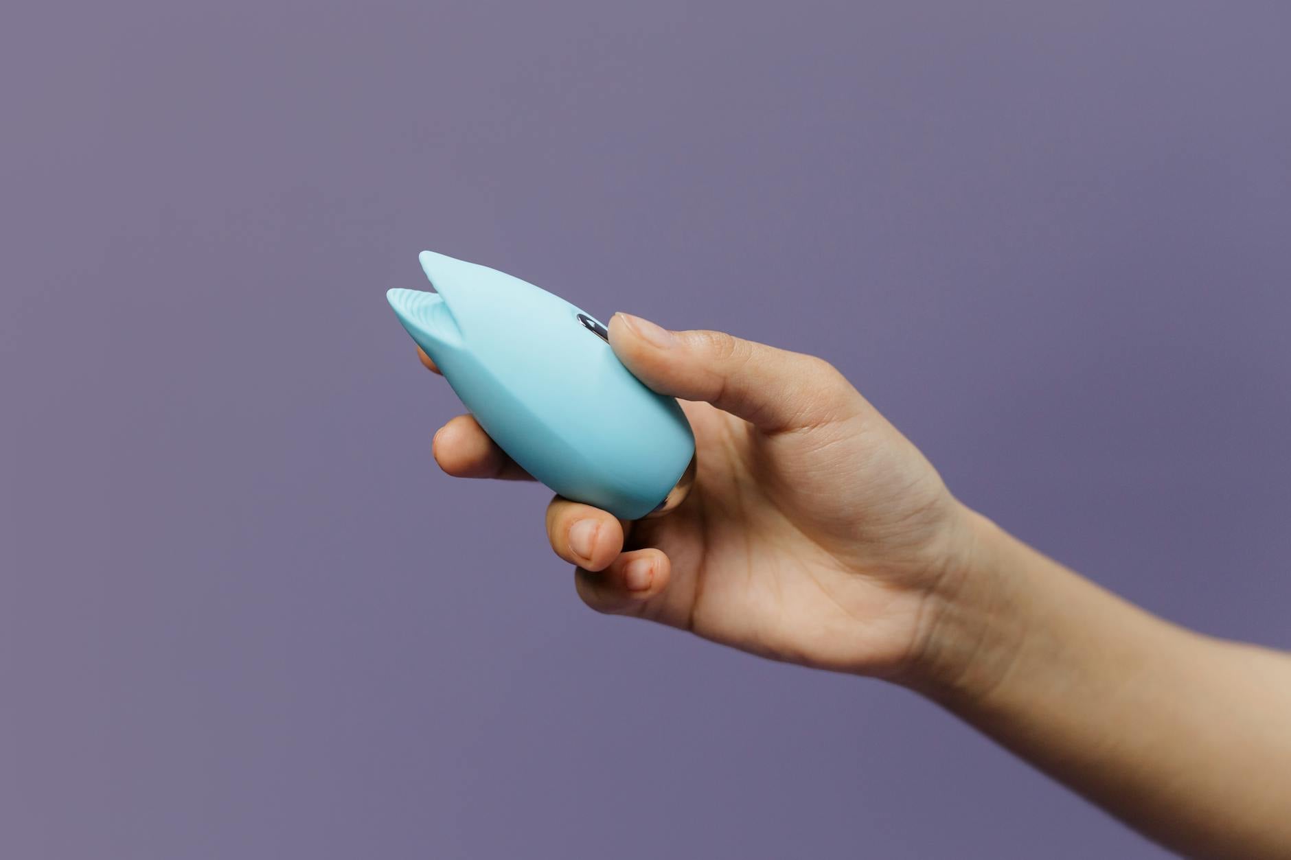 Ein blauer Silikonvibrator in der Hand auf violettem Hintergrund, Symbol für Selbstliebe und sexuelle Autonomie
