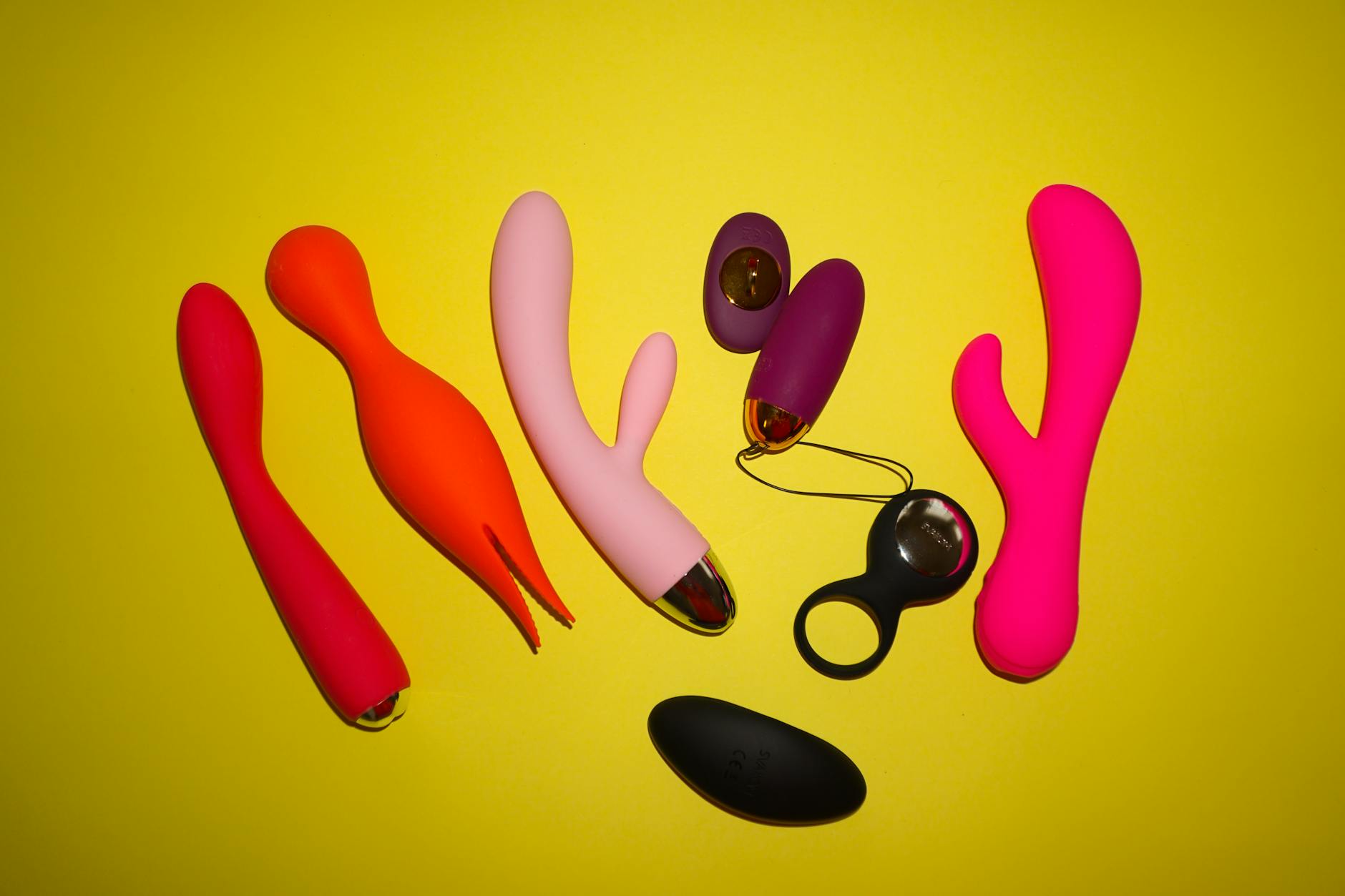 Colorful vibrators arranged on bright yellow background, including air-suction style toys